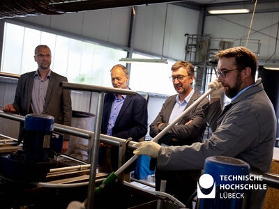 Dr. Johannes Oelerich (MELUND), Prof. Matthias Grottker und Vizepräsident Frank Schwartze der TH Lübeck schauen Dr. Kai Wellbrock bei einer Probenentnahme zu. Foto: TH Lübeck