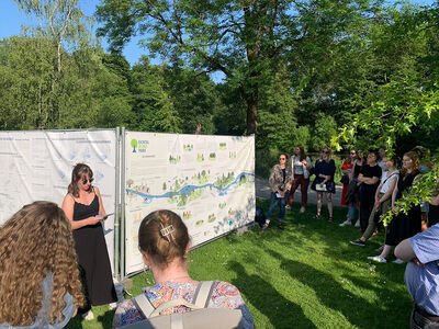 Personen stehen um Banner die an im grünen stehenden Bauzäunen angebracht sind