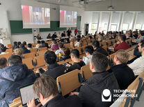 Studierende sitzen im Hörsaal und gucken auf das vorne sitzende Begrüßungskomitee