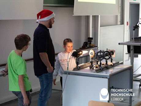 Ein Professor und sein junger Helfer zeigen einer Schülerin anhand eines Experiments, warum es im Winter bei uns kalt ist