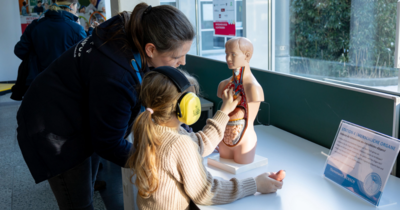 Hier sieht man eine Mutter mit ihrer Tochter an einer Puppe, bei der man den Sitz der Organe erkennen kann