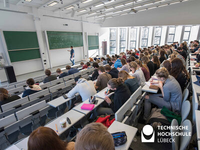 Bild zeigt viele Personen in einem Hörsaal die alle nach vorne zur Tafel gucken