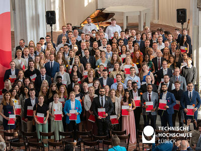 Eine große Gruppe von über 100 Studierenden stehen in der Kirche und halten ihre Zeugnisse hoch 