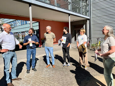 Sechs Personen stehen in einem Halbkreis vor einem Gebäude