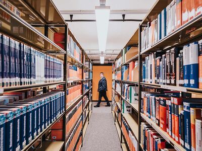 Auf diesem Bild sieht man links und rechts Bücherregale, die nach hinten weg spitz zulaufen, in der Mitte läuft ein Mann durch 