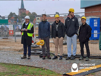 5 Personen stehen auf einer Baustelle und im Hintergrund Sand und Bauzäune