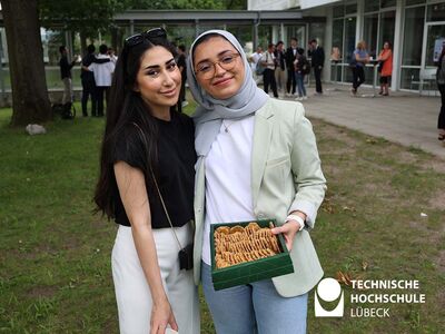 Zwei im grünen stehende Studentinnen halten Box mit Gebäck