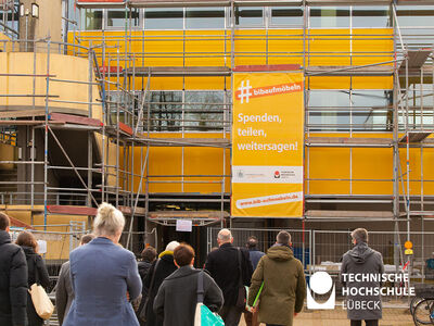 Bild zeigt mit Gerüst verkleidete Bibliothek mit Plakat und der Aufschrift Spenden, teilen, weitersagen