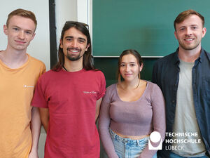 International Studierende stehen vor einer Tafel und lächeln für die Kamera