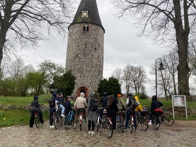 Studierende auf Fahrrädern stehen vor einem Steinturm