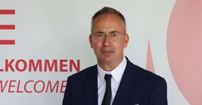 Ein Mann in einem Anzug mit Krawatte vor einem Banner.