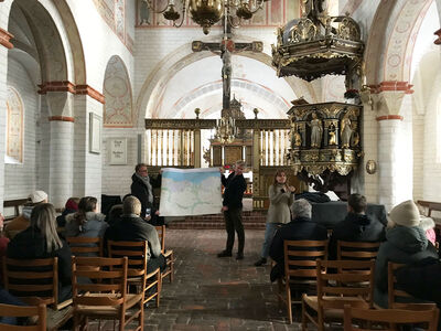 Teilnehmende sitzen in der Kirche und zwei Männer halten vorne Landkarte